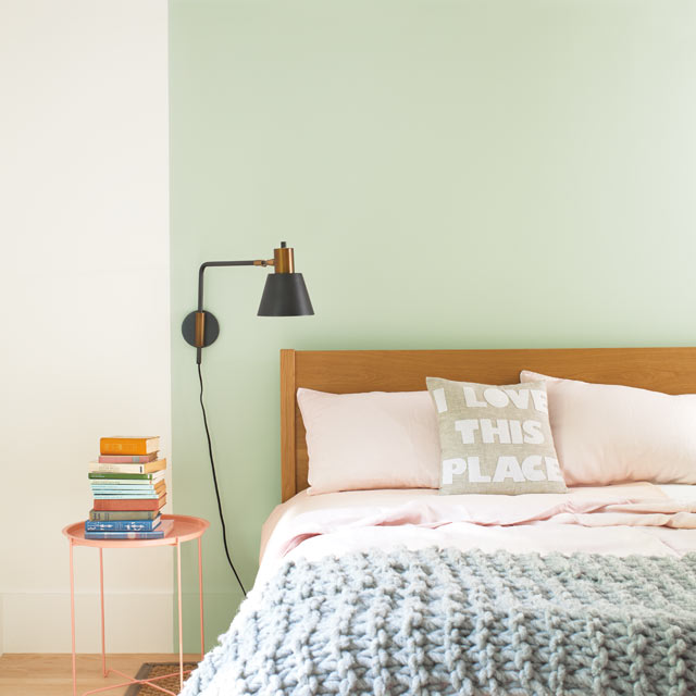 A bed set against a light green feature wall A bed set against a light green feature wall
